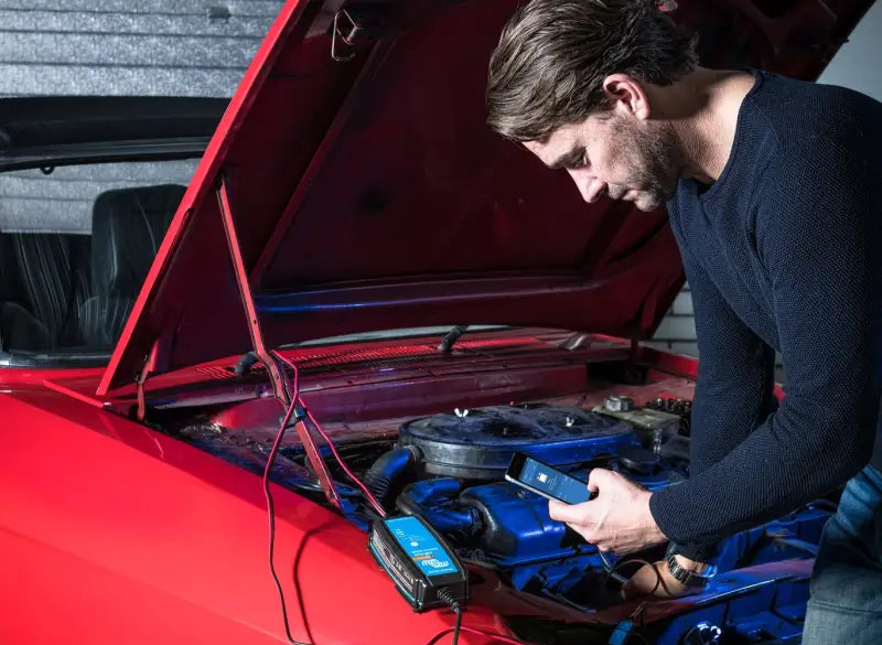 Man using Blue Smart IP65 Charger on car engine for lithium battery maintenance